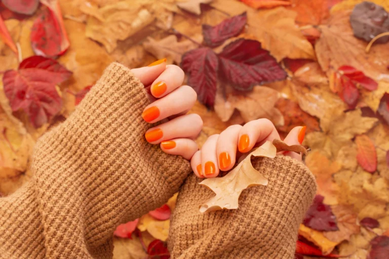 female hands with orange manicure background autumn leaves