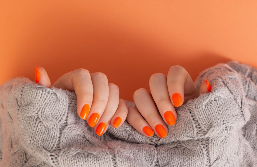 female hands with orange manicure orange background 1