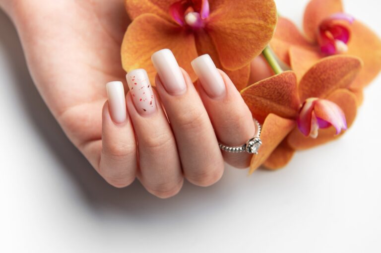 woman hand showing stylish trendy nude manicure holding orange orchid flowers