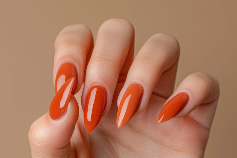 womans hand with long almond shaped nails painted with bright orange nail polish